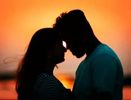 A close-up silhouette of a couple against a warm sunset sky, focusing on their connection.