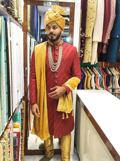 A groom trying on his red and gold sherwani in the studio. This classic combination is always a favorite for traditional Indian weddings.