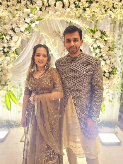 Standing before a beautiful floral arch, this couple looks elegant. His patterned Indo-Western sherwani in brown tones matches her embellished lehenga perfectly.