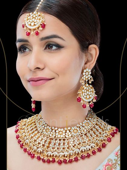 Accessorize your wedding outfit with this gorgeously crafted Polki Kundan bridal necklace set. The red beads add a traditional pop of color, and the set includes a matching maang tika.