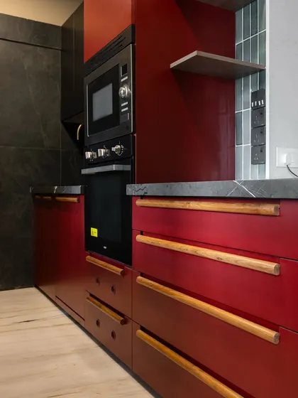A close-up of the integrated appliances in the Marsala red kitchen. The sleek black finish of the oven and microwave complements the deep red cabinetry and dark stone, creating a seamless and modern look.