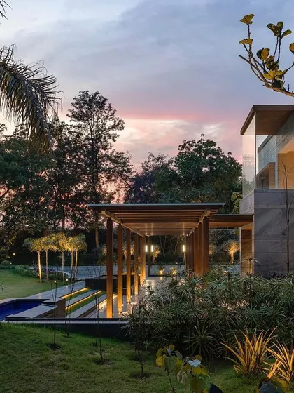 A view of the farmhouse at dusk, with the warm colors of the sunset reflecting on the building. The design seamlessly integrates water features and lush greenery with the modern stone and wood structure.