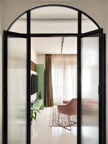 A direct view through the arched, fluted glass partition, offering an inviting glimpse into the colorful and contemporary living room beyond.