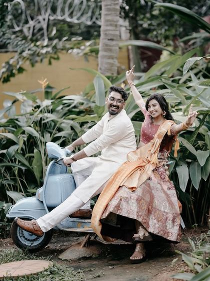 A fun and playful shot of a couple on a retro blue scooter, surrounded by lush greenery, perfect for a casual and quirky pre-wedding theme.