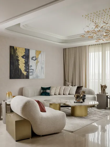 This living area is a study in soft sculpture and layered neutrals. A curved bouclé chaise and a long, low-slung sofa are arranged around marble coffee tables, creating a space that feels both contemporary and timelessly comfortable.