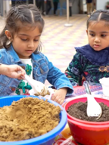 Two girls engaged in a sensory play activity with sand and soil during Meher's mermaid-themed birthday party.