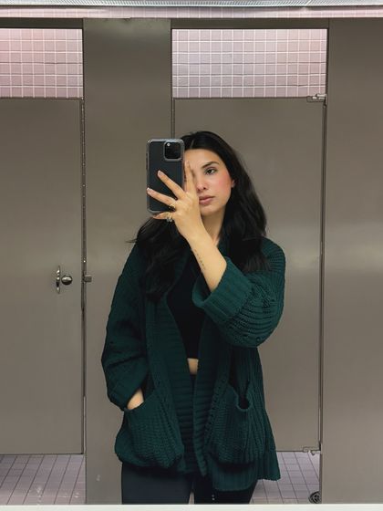 A bathroom mirror selfie showing a cozy green cardigan, perfect for a casual day on campus. This raw, unpolished style feels very authentic.