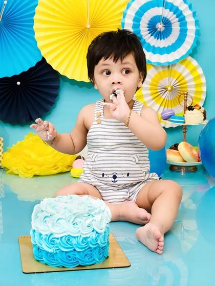 A baby boy enjoys his blue-themed cake smash, getting his first taste of birthday cake.