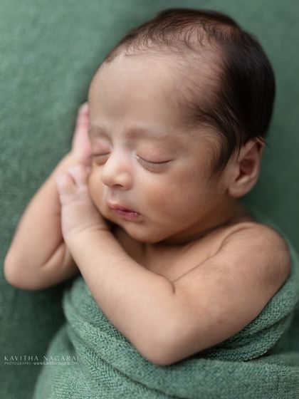A nine-day-old newborn in a classic curled-up pose, wrapped in a green swaddle. The simplicity of this shot makes it truly timeless.