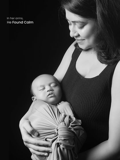 A powerful black and white portrait of a mother holding her sleeping baby. The dark background emphasizes the light on their faces and the feeling of calm and safety in her arms.