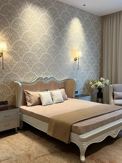 We designed this parent's room in Ambala with a touch of classic elegance. The bed features a beautifully carved frame with rattan detailing, complemented by a delicate patterned wallpaper and traditional wall sconces.