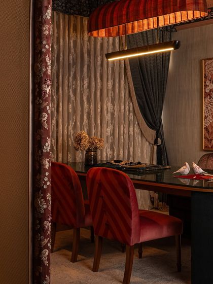 A view from the side, showing the striped red velvet chairs at the client interaction table. The embroidered fabric on the archway frames the scene, demonstrating how every surface is an opportunity for detailed, narrative-driven design.
