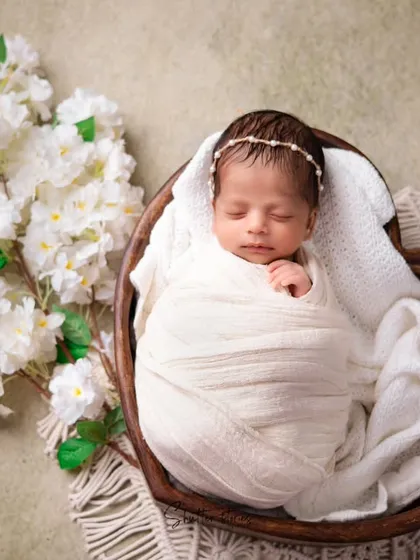 An elegant, all-white setup featuring a heart-shaped wooden bowl and white flowers. This monochromatic style creates a pure and timeless newborn portrait.