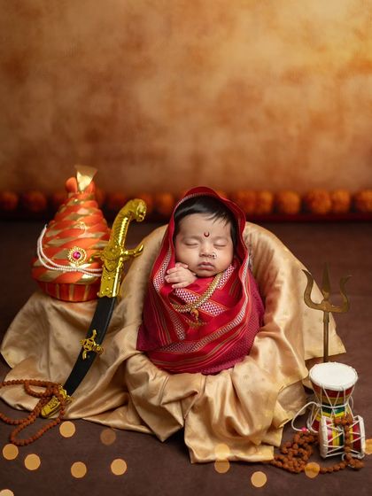 A full view of the regal setup, with the baby wrapped in red and gold, surrounded by symbolic props like the pheta, sword, and trishul against a warm, earthy backdrop.