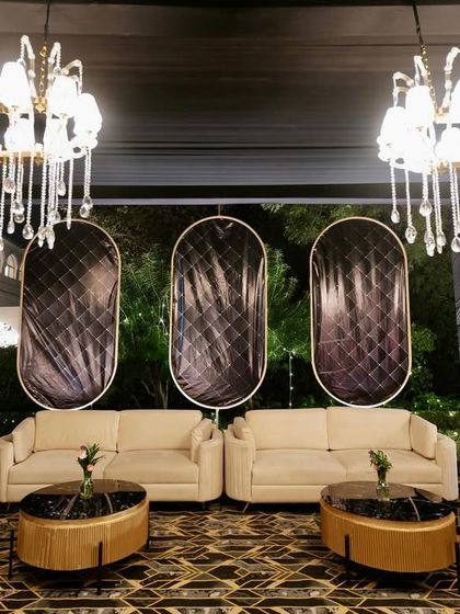 A chic Art Deco-inspired lounge area, with quilted black backdrops, cream-colored sofas, and modern chandeliers.