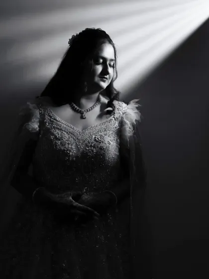 A beautiful black and white portrait of a bride in her reception gown. The soft, directional light creates an elegant and serene mood, highlighting the delicate details of her dress.