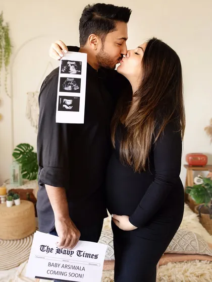 A classic pregnancy announcement photo. The couple holds up their ultrasound pictures and a custom "Baby Times" newspaper.