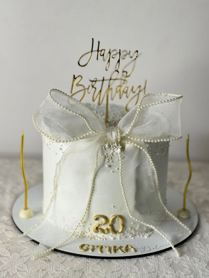 A classic white-on-white design for a 20th birthday. The cake is adorned with a delicate, handcrafted ribbon bow with pearl details, giving it a timeless and elegant feel.