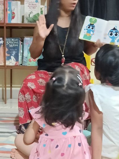 A storyteller shows a book with vibrant, modern illustrations, keeping the content fresh and visually appealing for the children.