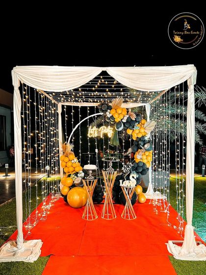 A "Let's Party" setup perfect for any celebration. This outdoor canopy is decorated with fairy lights, a red carpet, and a stylish black and yellow balloon arch, creating an inviting party space.