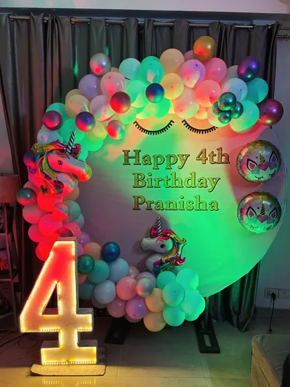A dreamy unicorn theme for a 4th birthday. The circular backdrop with sleepy eyes, surrounded by a rainbow pastel balloon arch and a light-up number '4', creates a whimsical look.