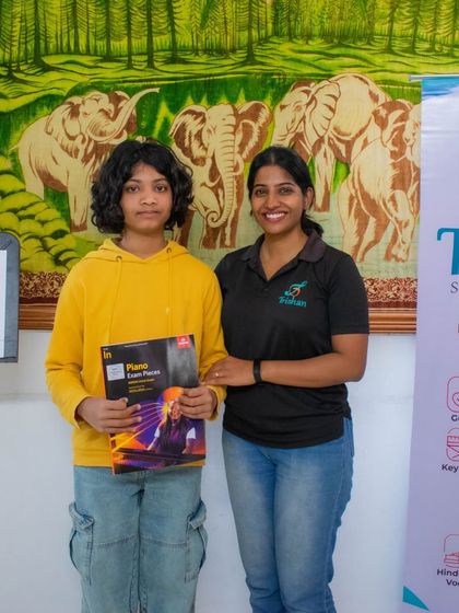 A student in a yellow hoodie holds her ABRSM piano exam book.