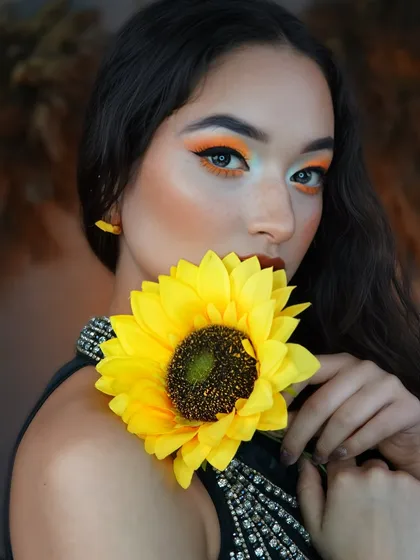 This creative pose uses the sunflower to complement the makeup, highlighting the vibrant color story and artistic direction.