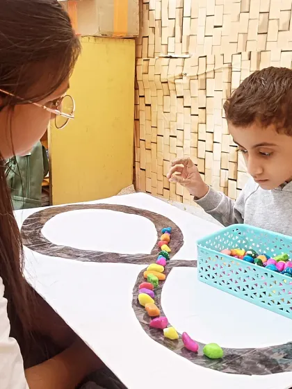 During an ABA therapy session, a child carefully places colorful stones along a winding path. This activity enhances fine motor precision, concentration, and hand-eye coordination.