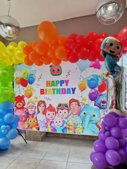 A colorful Cocomelon first birthday party with a rainbow balloon arch and a large printed backdrop featuring all the characters.
