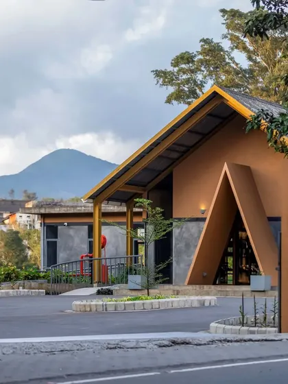 The entrance to the Teyla tea shop, where a prominent A-frame structure invites visitors into the experience center, set against the backdrop of the Idukki hills.