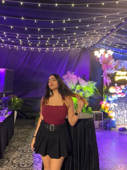 A full-length shot of the red and black outfit at a party. The fairy lights and event decor create a festive mood.