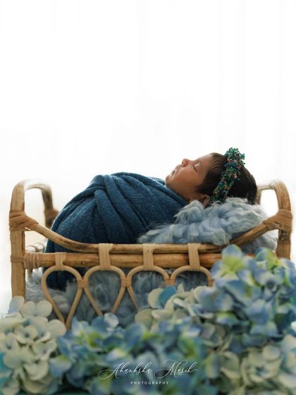A side view of this peaceful sleeper, nestled in a beautiful rattan crib. The blue tones of the wrap and flowers create a serene and cohesive look for this newborn portrait.