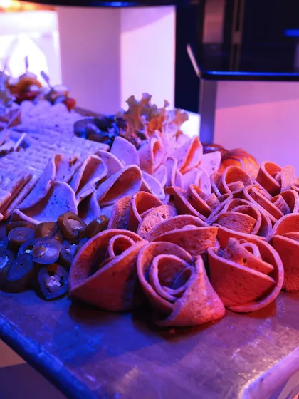 A beautiful charcuterie board featuring artfully arranged cold cuts shaped like roses, served with jalapeños and crackers.