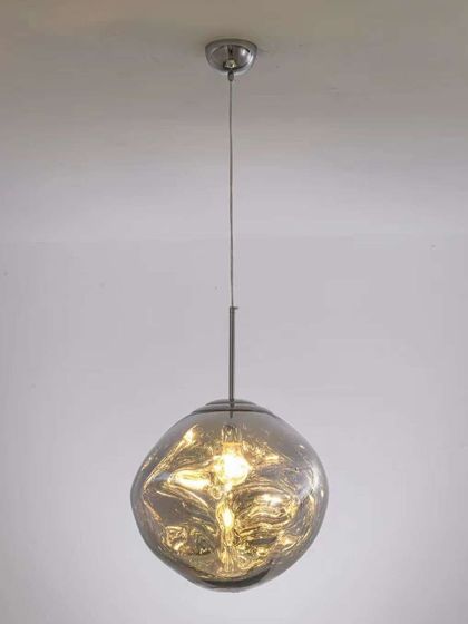 A pendant light with a molten, irregular-shaped smoked glass shade. Each piece is unique, adding an organic and artistic touch.