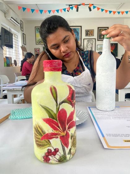 A participant works on her decoupage bottle, showing the before and after of the transformation.