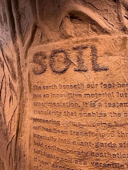 A close-up of the 'Soil' text and narrative, etched directly into the earthen wall. This technique integrates the story physically into the material it describes.