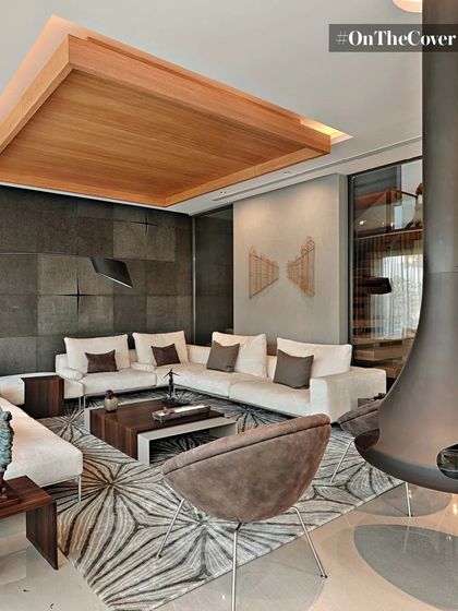 This living area showcases our approach to minimalist luxury. A suspended fireplace acts as a sculptural element, complemented by a geometric rug, a warm wood ceiling, and a textured stone wall to create a space that is both modern and inviting.