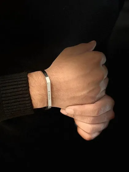 A close-up of a man's hands against a dark background, with a silver cuff bracelet adding a point of contrast and light.