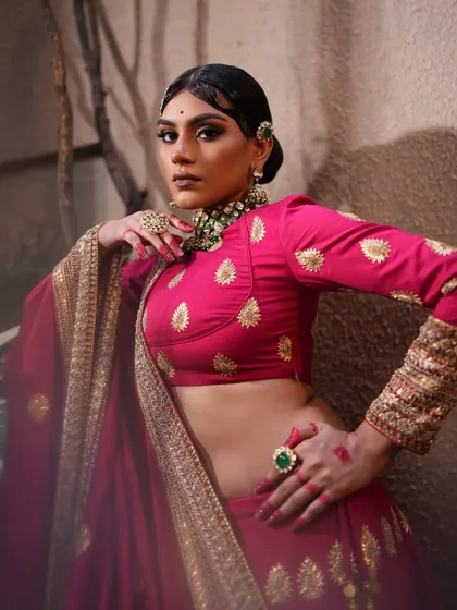 A powerful pose in a fuchsia pink lehenga. The styling is bold and artistic, with a focus on the dramatic makeup and traditional jewelry.