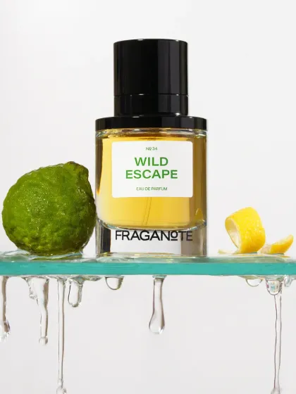 A 'Wild Escape' perfume bottle sitting on a glass shelf with dripping water. This creative shot visually communicates a sense of dripping freshness and citrus notes.