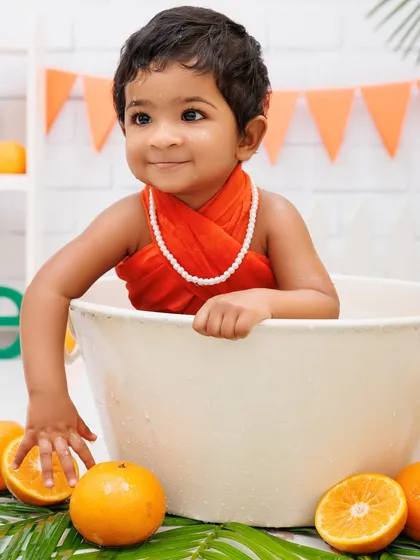A serene moment during a tub splash session, with a baby girl surrounded by fresh oranges.