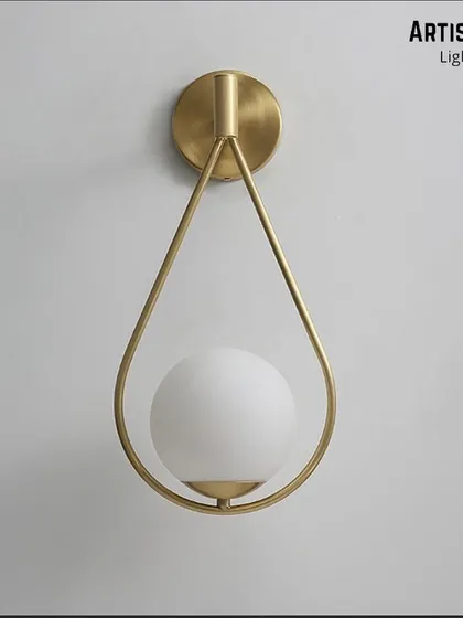 Inspired by a falling drop of rain, this wall light features a frosted white globe delicately held within a teardrop-shaped brass frame. It is a poetic and graceful addition to any contemporary space.