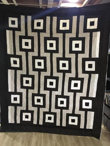 A modern, graphic quilt with a repeating pattern of interconnected squares in black, white, and grey.