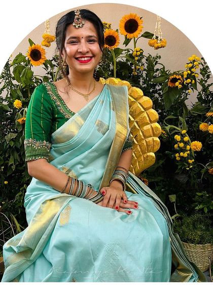 A happy client in a beautiful light blue saree with a traditional gold border. The ensemble is elevated by a custom-designed, richly embroidered green blouse.