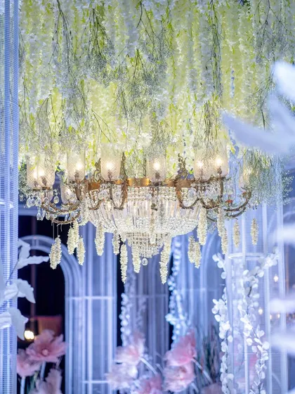 A close-up of a classic crystal chandelier surrounded by cascading white wisteria. This detail shot highlights the timeless elegance of combining classic lighting with delicate floral elements.