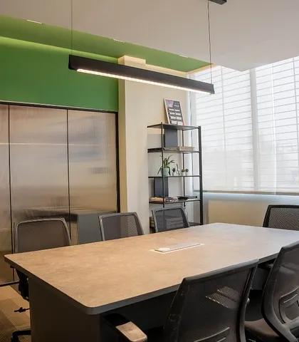 The conference room is designed to be bright and airy, with large windows and sheer blinds to control natural light. The linear pendant light provides excellent task lighting over the concrete-finish tabletop.