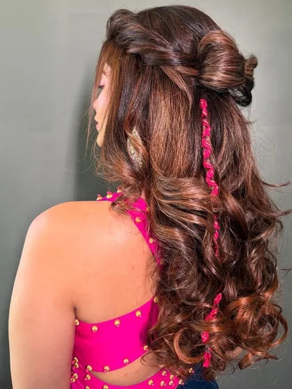 A fun and playful half-updo with a top knot and a pop of color from a pink braid, perfect for a vibrant Haldi or Mehendi party.