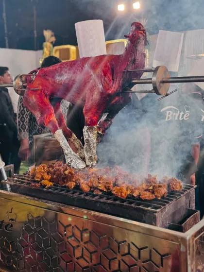 A close-up of the whole roasted goat, showcasing its perfectly cooked, crisp skin and the smoky ambiance of the live grill.