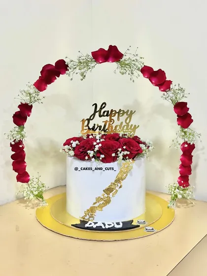 A stunning birthday cake with a floral arch made of fresh red rose petals and baby's breath. The gold leaf detail adds a touch of luxury.