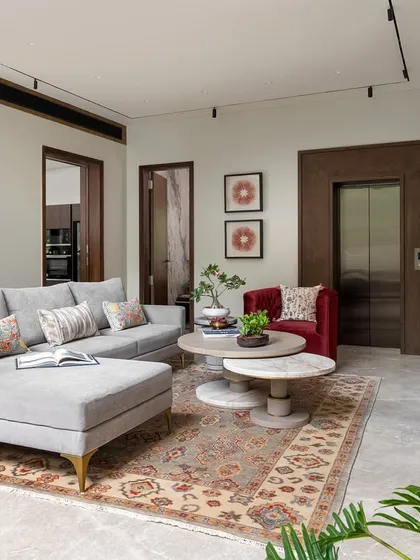 The family lounge is designed for comfort, with a plush sectional, a soft Persian rug, and a bold red accent chair. The wood-clad elevator shaft adds a warm, architectural element to the room.
